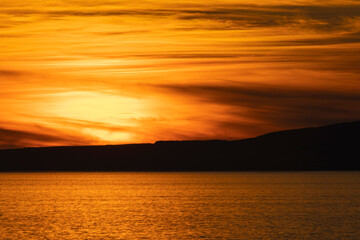 Fototapeta premium Golden sunset over Isle of Arran in the Firth of Clyde sea with band of dark cloud in sky