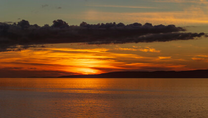 Golden sunset over Isle of Arran in the Firth of Clyde sea with band of dark cloud in sky