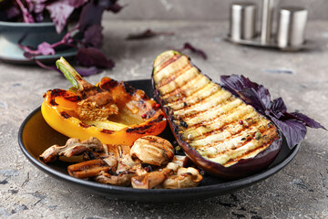 Plate with grilled vegetables and basil on grey background