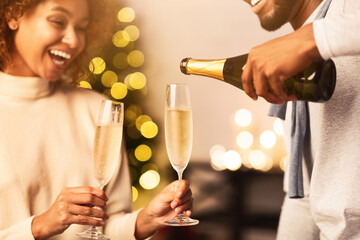 Man pouring champagne into glasses, celebrating Christmas together with girlfriend at home