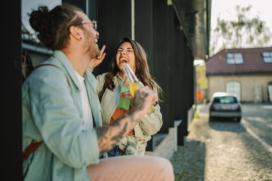 Young alternative couple sitting on street and having bottles of drinks