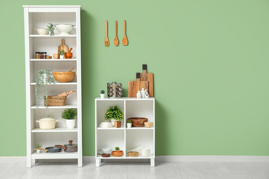Modern shelving unit with dishes and houseplant near green wall in kitchen