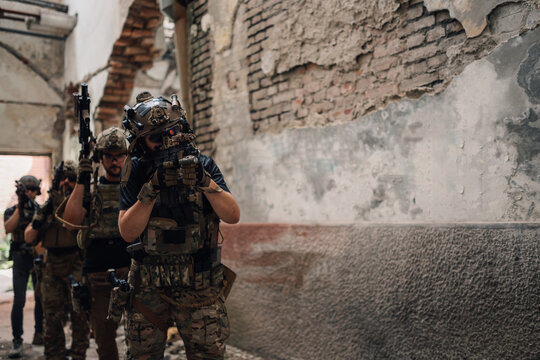 Team of four airsoft teammates with rifles in action at old facility.