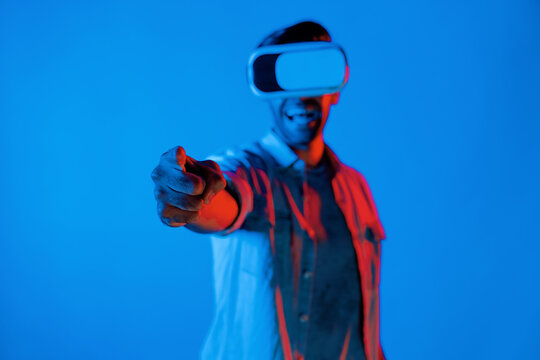 Smiling gamer wear virtual reality glass while pointing at camera. Happy caucasian man with VR goggles and casual cloth using future innovation technology to enter virtual world simulation. Deviation. - Powered by Adobe
