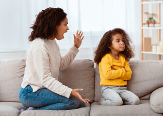 Angry Afro Mother Shouting At Offended Daughter Sitting On Couch At Home. Family Problems, Quarrels And Aggression