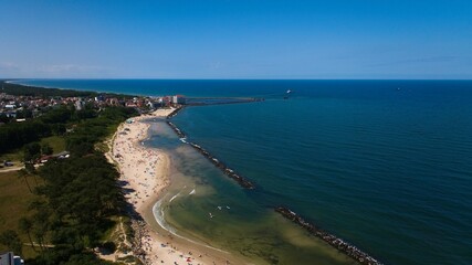 Golden beach, calm Baltic waters, sunbathers, swimmers, and ships from Darłowo port, captured by a...