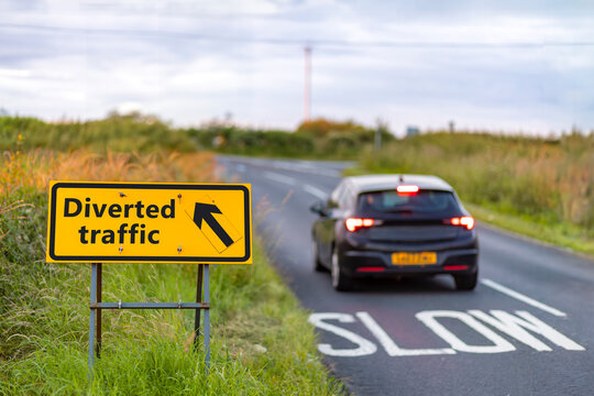 Car passing yellow diverted traffic sign at slow bend on country road