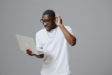 African man using laptop, excited expression, casual white shirt, technology engagement, grey background, modern lifestyle, joyful interaction, digital connection