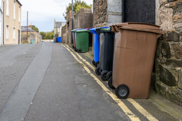 UK waste wheelie wheeled bin stored along roadside with double yellow lines and garage entrances on...