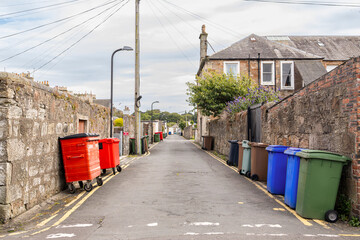 UK waste wheelie wheeled bin stored along roadside with double yellow lines and garage entrances on...