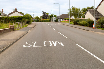Bend in village road with SLOW painted on the tarmac surface and footpath pavement and houses...