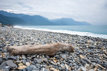 A piece of driftwood lies on a rocky shore, with ocean waves and mountains at Qixingtan Beach, Hualien, Taiwan