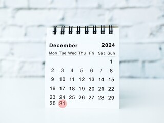 A modern desktop calendar for December 2025 with the 31st highlighted in red, sitting on a white table against a white brick wall. New year's eve or end of year date
