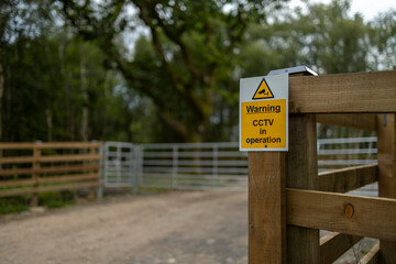 Entrance to farm property protected by CCTV surveillance in operation warning sign on wood fence