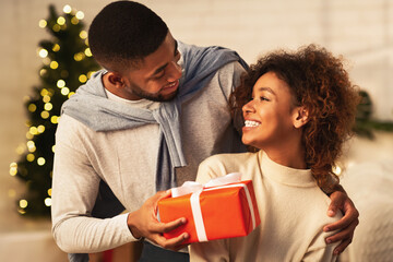 Happy New Year. Afro man giving Christmas present to wife, celebrating holidays at home