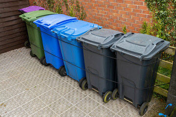 Plastic Waste Recycling Wheelie Bins lined up and secured in a UK garden storage area beside house...