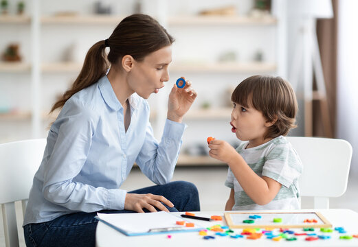 Female speech therapist curing child's problems and impediments. Little boy learning letter O with private English language tutor during lesson at office