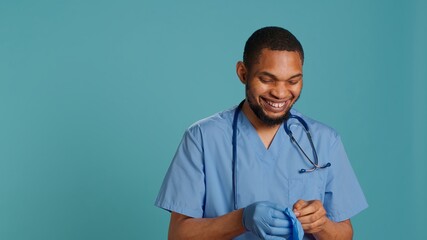 Male nurse putting on rubber gloves, preparing for surgery, isolated over studio background. Practitioner wearing sterile surgical equipment before medical exam, camera A