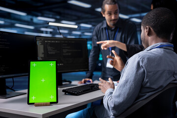 Multiethnic team using green screen tablet to oversee servers used for managing databases. Diverse...