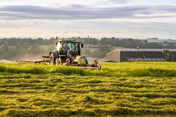 DRONGAN, UK - JULY 22, 2024: Farm tractor and mower cutting hay field at sunset