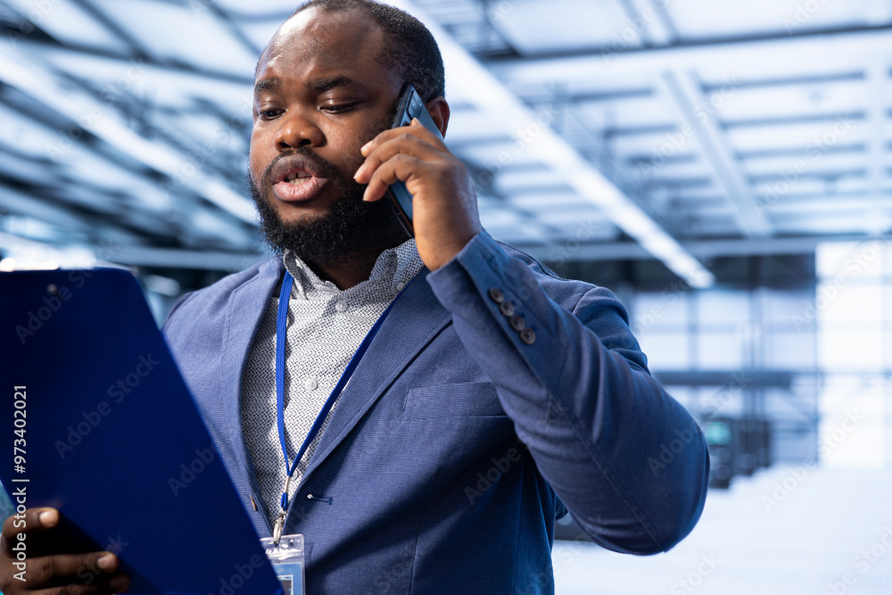 Poster african american man maintaining accurate documentation of data center systems, chatting on phone wi
