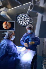 Experienced surgeon in mask adjusting tools during operation