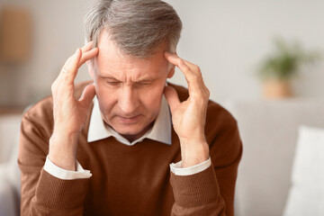 Headache. Senior Man Suffering From Migraine Touching Temples Sitting On Sofa At Home. Selective...