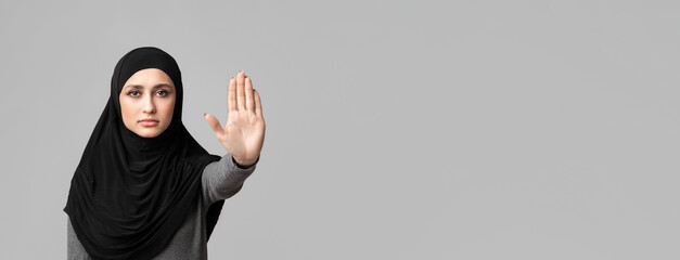 No abuse and discrimination. Muslim woman in hijab making stop gesture with her hand, covering her face with open palm over gray background