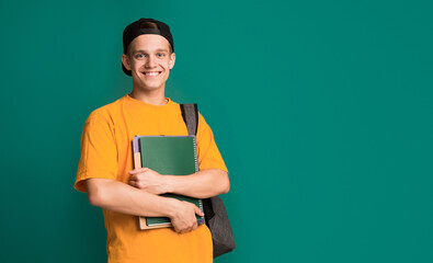 Happy student with books and backpack over turquoise background, copy space