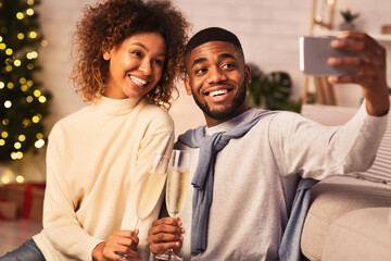 Cheerful african-american couple taking selfie on New Year Eve, drinking champagne