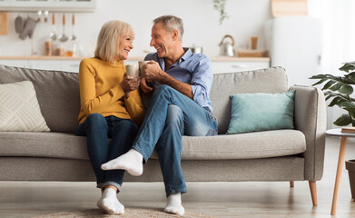 Happy Senior Couple Drinking Coffee Holding Mugs With Hot Drink And Smiling To Each Other Sitting...