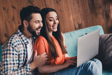 Photo of cheerful cute young couple cuddle sit sofa eshopping enjoy weekend have fun buy new apartment indoors inside house home