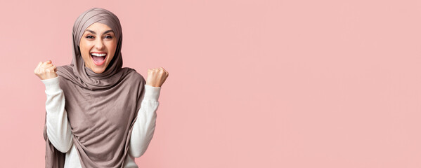 Joy Of Victory. Happy Muslim Woman in Hijab Shaking Fists Celebrating Success Over Pink Studio...