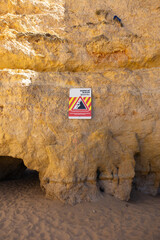 Rockfall warning sign on Algarve's cliffs, Portugal. The sign urges beachgoers to maintain a safe distance from the cliff to prevent potential accidents due to falling rocks