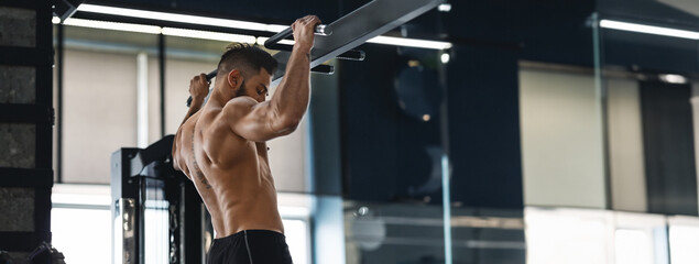 A man exercises by doing pull-ups at a well-equipped gym, focusing on building upper body strength, copy space