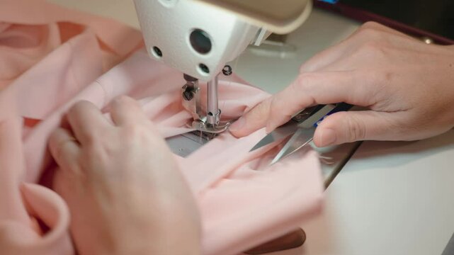 Close-up of the sewing machine, stitching stitching. Sewing production. Hands seamstress stitching clothes. Tailoring production. The seamstress cuts the thread with scissors. High quality 4k footage