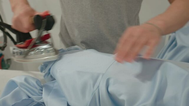 Close-up view of a female worker ironing clothes. Dry cleaner, laundry, industrial factory, clothing production. Professional steaming of clothes. High quality 4k footage