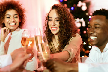 Celebrating New Year. Diverse Friends Toasting And Clinking Glasses Smiling Sitting At Celebratory Table Indoor. Selective Focus