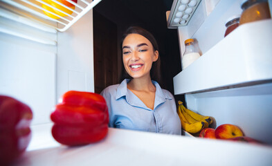 Healthy nutrition. Young housewife choosing vegetable for dinner in fridge, view from inside