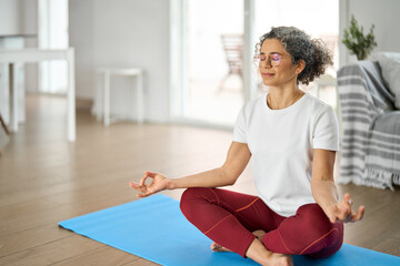 Happy healthy middle aged woman meditating at home. Serene mindful mature older lady in her 50s...