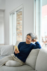 Smiling middle aged woman wearing glasses looking at cell phone doing ecommerce mobile shopping...