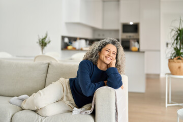 Happy relaxed 50 years old woman laying on sofa at home looking away. Smiling middle aged lady...
