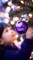 Naklejka premium A young child hangs a Christmas bauble on the tree. 