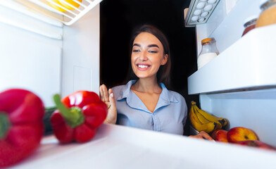 Clean nutrition. Happy woman taking fresh vegetables from fridge, view from inside