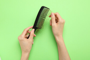 Woman taking her lost hair from comb on light green background, top view. Alopecia problem