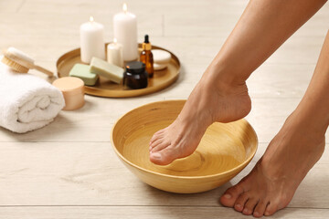 Woman soaking her feet in bowl with water on floor, closeup. Body care
