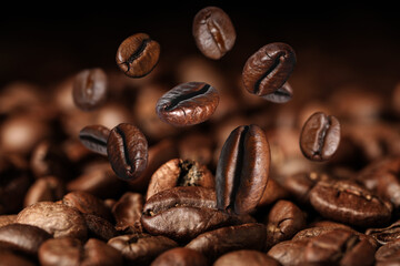 Roasted coffee beans falling on heap against black background, closeup