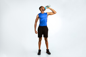 Stay Hydrated. Full length muscular afro man drinking water from bottle over yellow studio...