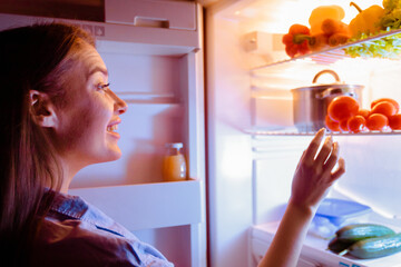 Healthy diet. Millennial housewife choosing vegetable for late dinner in fridge, free space