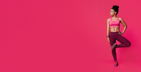 Fitness black girl warming up her body, stretching legs and looking at free space, red background